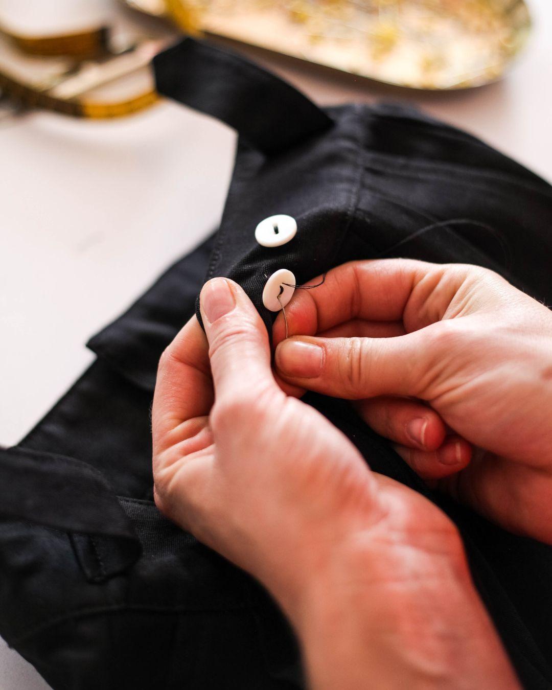 Hands sewing a corozo button onto black fabric