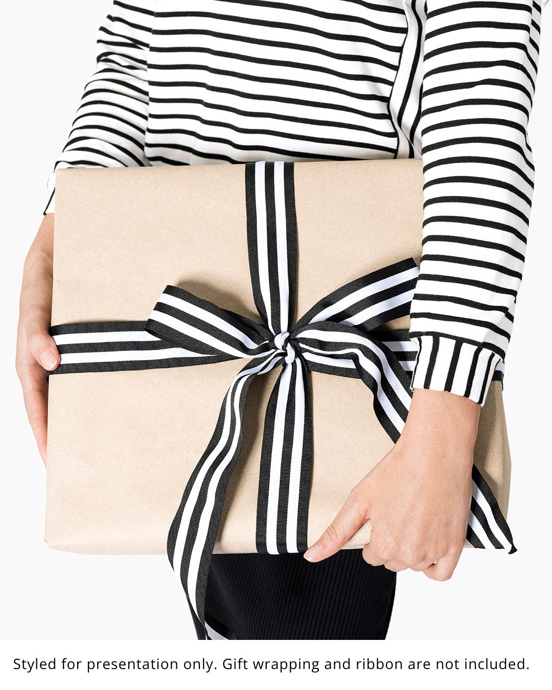 Woman in a black-and-white striped top holding a kraft-paper-wrapped box tied with striped ribbon. Gift wrapping and ribbon are not included. | Women's Mystery Clothing Box | Lacson Ravello